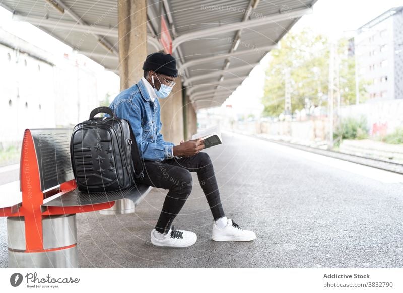 Ethnischer Mann liest Buch auf dem Bahnhof warten Zug Podest lesen Reisender Mundschutz Coronavirus Eisenbahn männlich ethnisch schwarz Afroamerikaner Ausflug