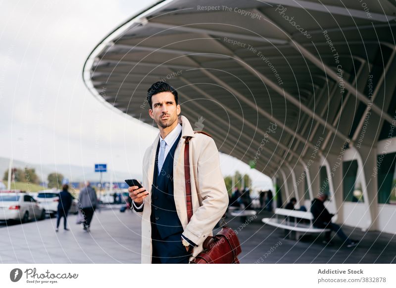 Nachdenklich Mann schaut weg in der Nähe von Flughafen mit Ihrem Telefon in der Hand Stehen trendy zuschauen Straße Stil Geschäftsmann Konzentration männlich