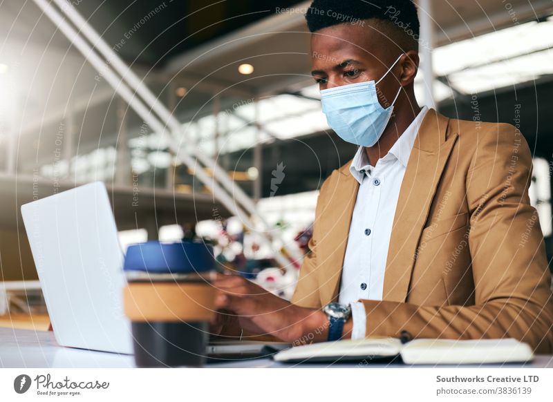 Junger Geschäftsmann mit Maske, der während einer Gesundheitspandemie am Laptop am heißen Schreibtisch im Büro arbeitet Business Gesichtsmaske Gesichtsbedeckung