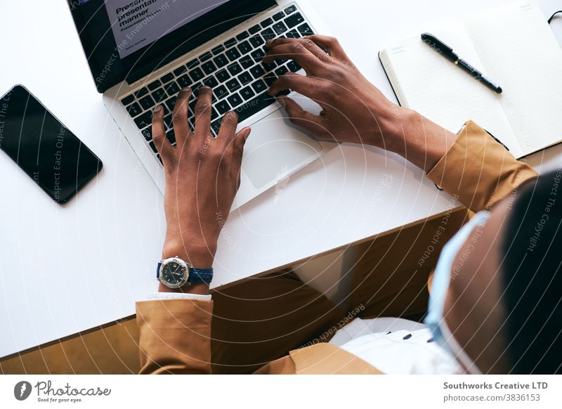 Überkopfaufnahme eines Geschäftsmannes mit Maske bei der Arbeit am Laptop am heißen Schreibtisch im Büro bei einer Gesundheitspandemie Business Gesichtsmaske