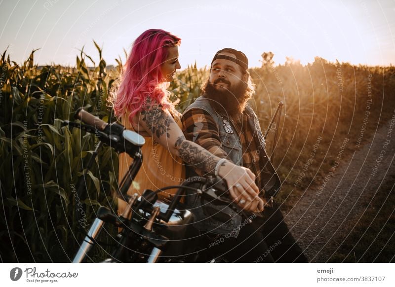 junges Paar mit Tätowierungen und pinken Haaren und Motorrad jugendlich paar liebe verliebt sonnenuntergang Draussen feld pinke haare Tattoo trendy Hipster Mann