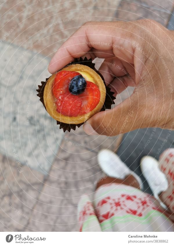 Frau hält eine kleine Süssigkeit in der Hand: Erdbeertartelette mit einer Blaubeere Dessert Erdbeere Erdbeeren Blaubeeren Frucht Lebensmittel Bioprodukte frisch