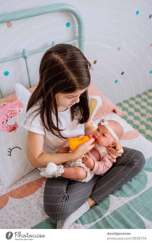 kleines Mädchen spielt Füttern ihrer Babypuppe Spielen Fütterungsflasche Nachahmungsspiel traditionelles Spielzeug Kind niedlich Zärtlichkeit Puppe schön