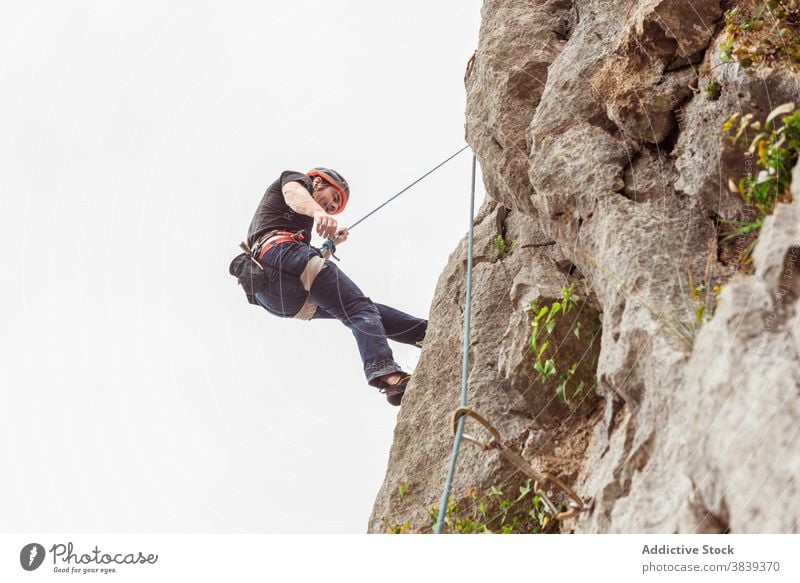 Männlicher Kletterer beim Aufstieg an einer steilen Felswand im Sommer Aufsteiger aufsteigen steile Klippe Mann Alpinist Berge u. Gebirge üben Klettern aktiv