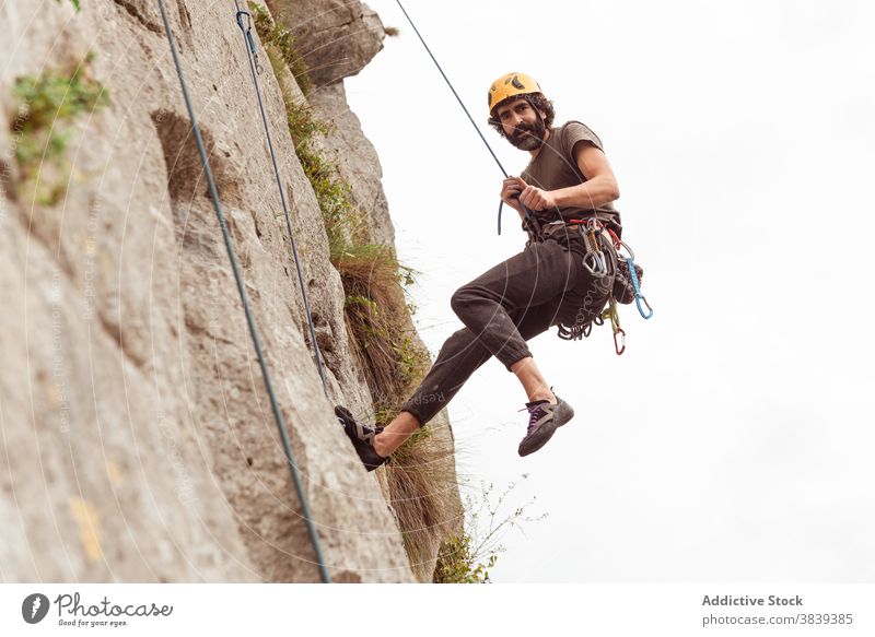 Männlicher Kletterer beim Aufstieg an einer steilen Felswand im Sommer Aufsteiger aufsteigen steile Klippe Mann Alpinist Berge u. Gebirge üben Klettern aktiv