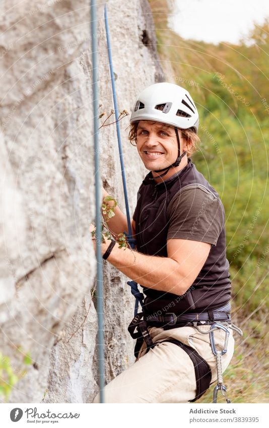 Starker männlicher Alpinist in Sicherheitsausrüstung beim Klettern am Felsen an einem sonnigen Tag Mann Bergsteiger Seil Gerät Berghang Berge u. Gebirge stark