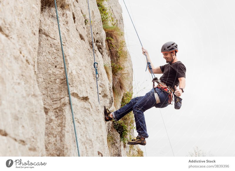 Starker männlicher Alpinist in Sicherheitsausrüstung beim Klettern am Felsen an einem sonnigen Tag Mann Bergsteiger Seil Gerät Berghang Berge u. Gebirge stark