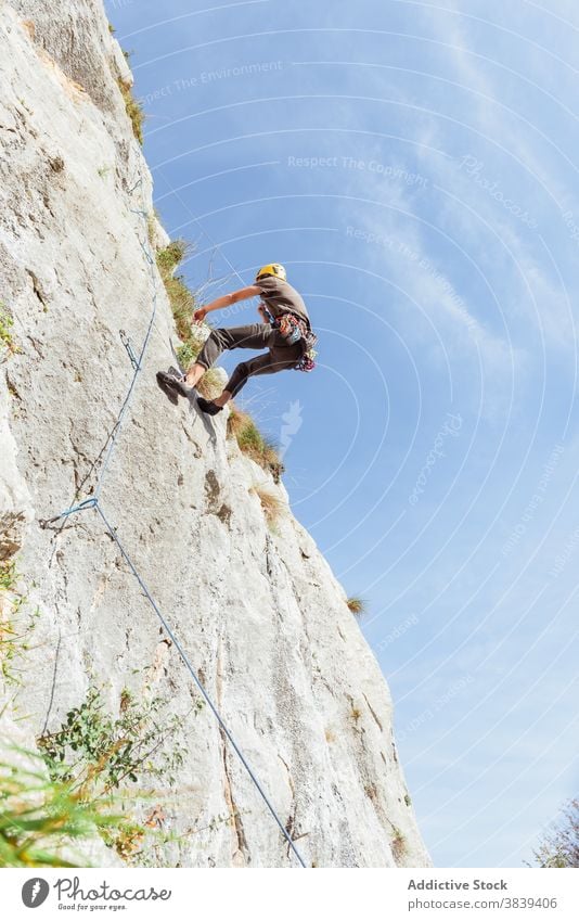 Männlicher Kletterer beim Aufstieg an einer steilen Felswand im Sommer Aufsteiger aufsteigen steile Klippe Mann Alpinist Berge u. Gebirge üben Klettern aktiv