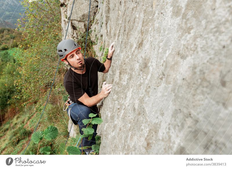 Männlicher Kletterer beim Aufstieg an einer steilen Felswand im Sommer Aufsteiger aufsteigen steile Klippe Mann Alpinist Berge u. Gebirge üben Klettern aktiv