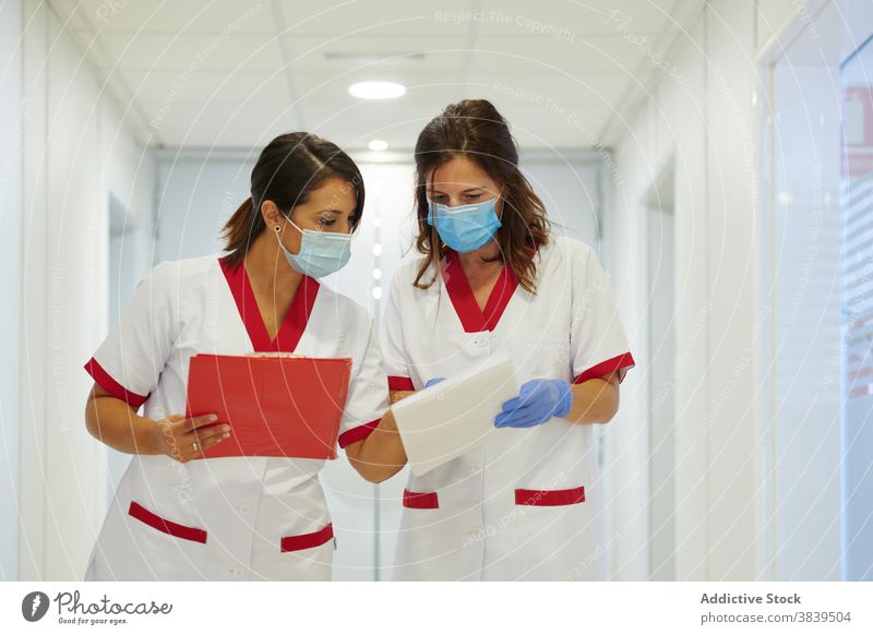 Anonyme Krankenschwestern in Uniformen mit Papieren interagieren in der Krankenhauspassage medizinisch Personal Beruf Spaziergang Durchgang Frauen