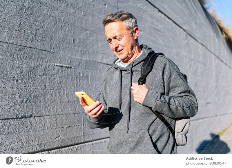 Senior im Ruhestand Mann mit Sportkleidung und Smartphone zu Fuß die Straße hinunter 60 ruhen Rhythmus Gesundheitswesen Fitness Training kardial alt Hals Pflege