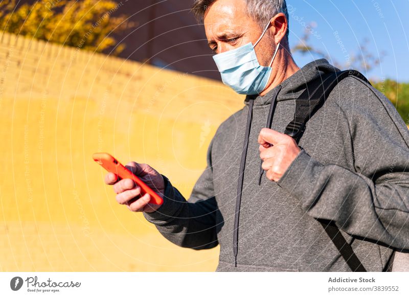 Älterer Rentner mit Gesichtsmaske, Sportkleidung und Smartphone geht die Straße entlang 60 ruhen Gesundheitswesen Fitness Training kardial alt Hals Pflege