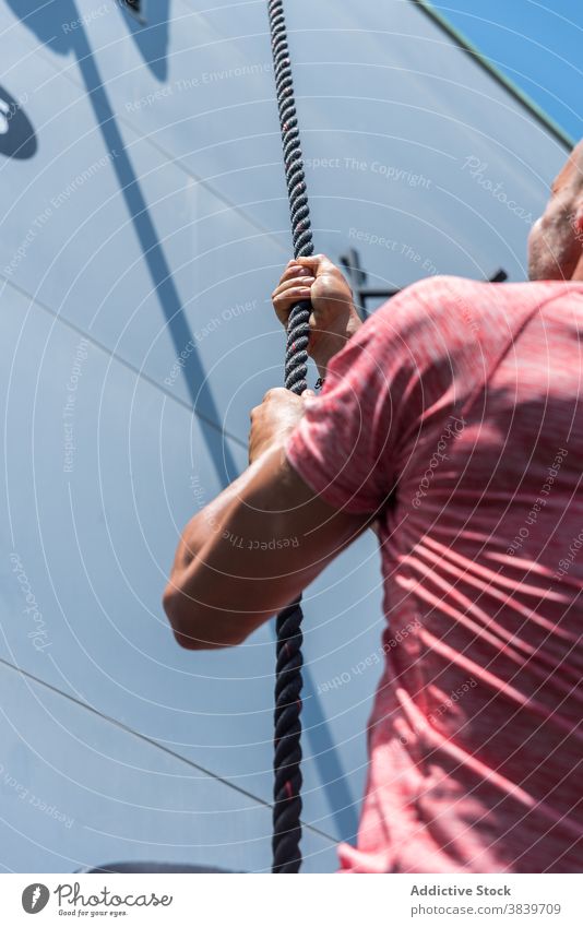 Ausdauernder Mann klettert beim Training am Seil Aufstieg Übung Sportler üben anstrengen stark männlich Athlet Gesundheit selbstbewusst Aktivität Bestimmen Sie