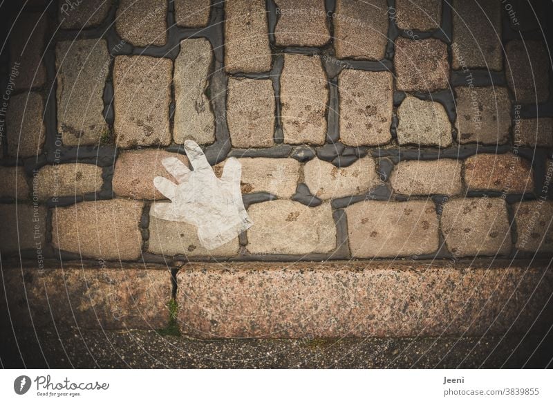 Ein Einmal-Handschuh aus Plastik liegt auf dem Kopfsteinpflaster Einmalhandschuh Plastikhandschuh Wegwerfgesellschaft Umweltverschmutzung Müll Umweltsünder