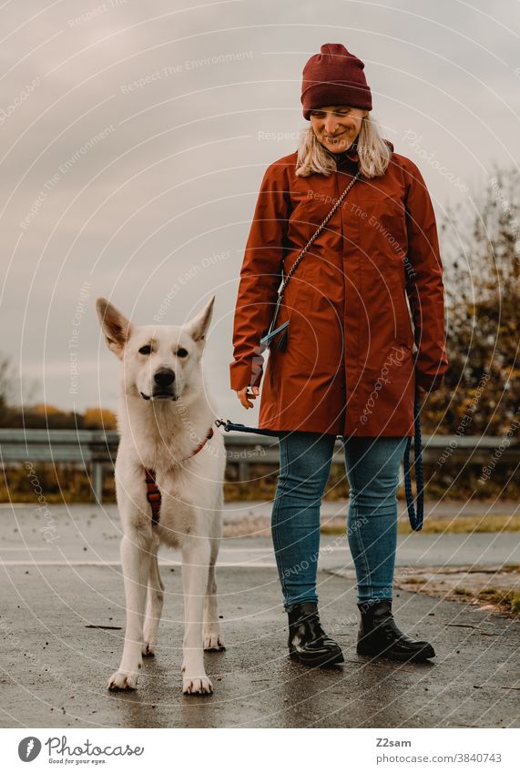 Junge Frau beim Gassi gehen mit weißem Schäferhund gassi gehen schäferhund spazieren zuneigung erziehung rot mütze herbst feld natur ländlich sitzen leine brav