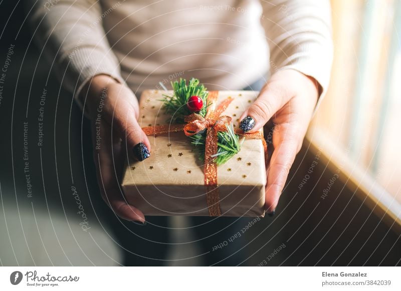 Junge Frauen mit Glitzernägeln, die eine Weihnachtsgeschenkschachtel halten und sie in der Kamera zeigen. Hände halten eine Neujahrsgeschenkschachtel, die mit Bastelpapier, Kiefernzweig, rotem Band und Sternen dekoriert ist. Konzept für Familiengeschenke.