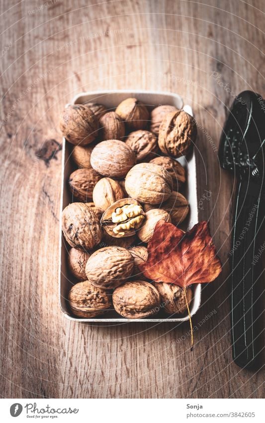 Ganze Walnüsse in einer Schüssel und ein Nussknacker auf einem braunen Holztisch. Walnuss rustikal Herbstlaub herbstlich Nahaufnahme Protein Blatt Schale lecker