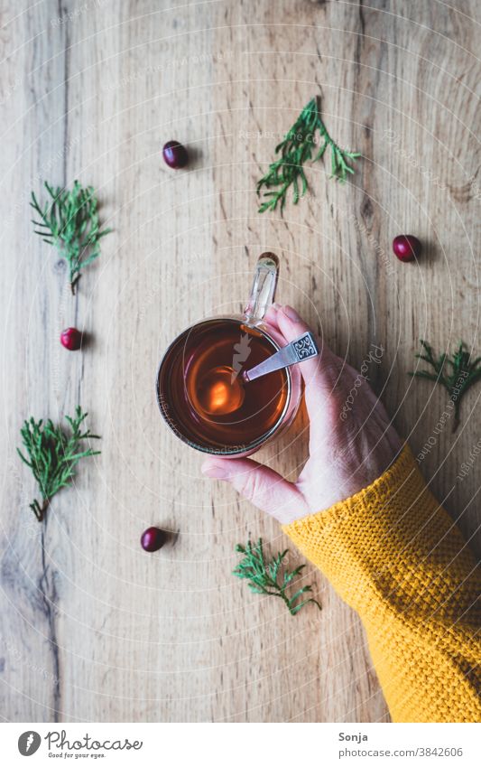 Weibliche Hand hält ein Glas Tee auf einem herbstlichen Hintergrund. Gelber Wollpullover, Teilabschnitt. Trinkglas Frau halten Hygge teepause Herbst Lifestyle