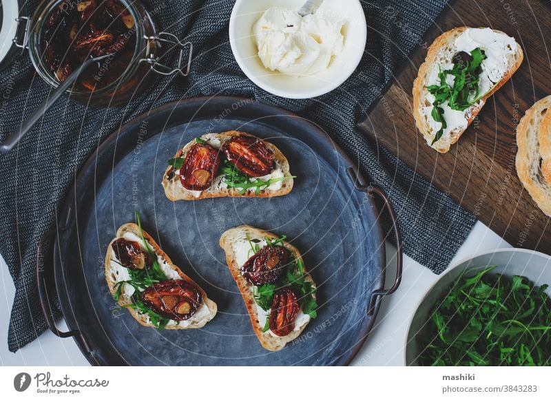 traditionelle italienische Bruschetta - Brottoast mit sonnengetrockneten Tomaten, Frischkäse, Olivenöl und Rucola. Belegtes Brot Lebensmittel Zuprosten Snack