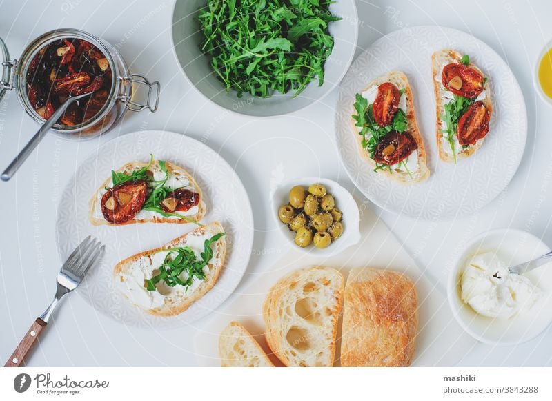 traditionelle italienische Bruschetta - Brottoast mit sonnengetrockneten Tomaten, Frischkäse, Olivenöl und Rucola. Belegtes Brot Lebensmittel Zuprosten Snack