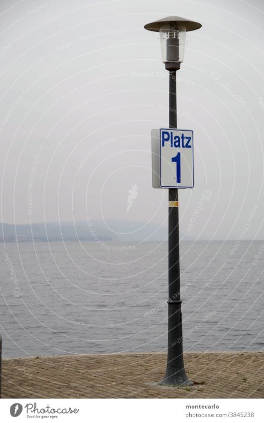 laterne mit schild platz 1 am fähranleger in uhldingen am bodensee angeschraubt weiß Hinweisschild Schriftzeichen Tag Zeichen Menschenleer Außenaufnahme