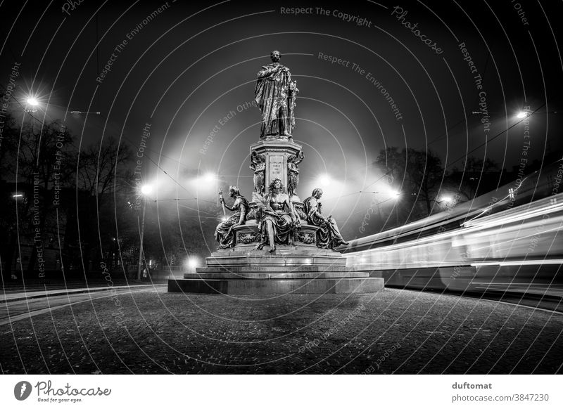 Schwarzweiß Foto mit Langzeitbelichtung eines Denkmals bei Nacht Schwarzweißfoto Straßenbahn Licht München Berufsverkehr Statue verschwommener hintergrund Abend