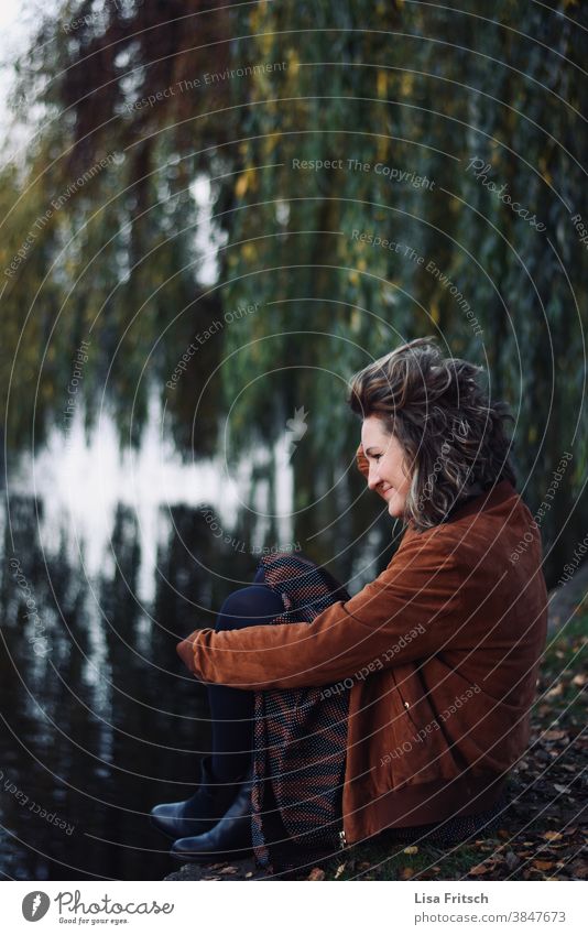 TRAUERWEIDE - FRAU -HERBST Herbst Trauerweide herbstlich Wasser Fluss sitzend Frau 30-45 Jahre Junge Frau Locken blond modern Spiegelung im Wasser Erwachsene