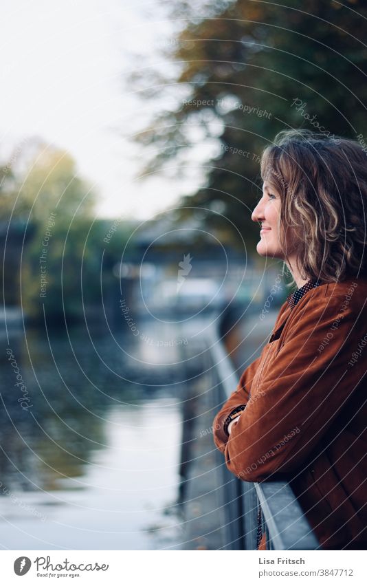 SCHÖNE AUSSICHT - GRINSEN Frau Locken anlehnen Wasser Spiegelung im Wasser Bäume Herbst herbstlich braun 30-35 Jahre alt grinsen fröhlich zufrieden