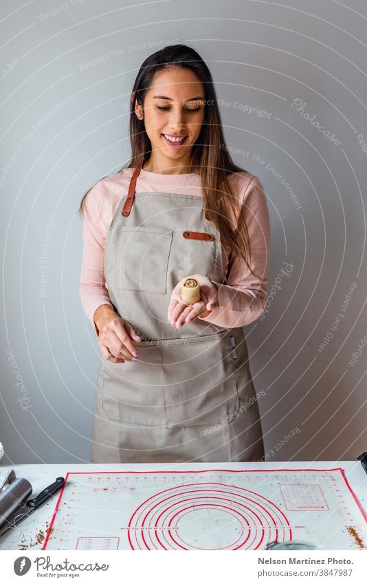 Hispanische Frau mit einer kleinen Zimtrolle in der Hand. Erwachsener Mann im Innenbereich Essen zubereiten Teigwaren Mehl Küchenchef Restaurant Beschäftigung