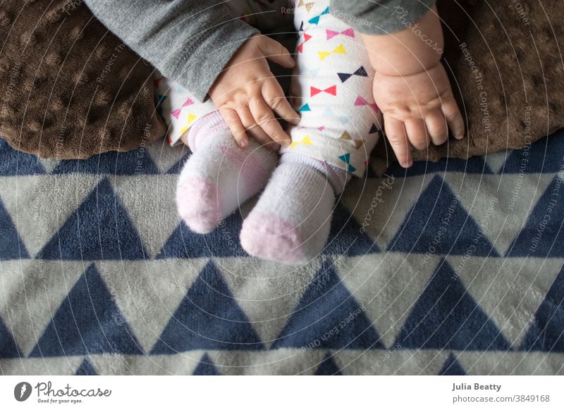 Baby, das nach den Füßen greift, Babyhände mit Grübchen, Decke und Hose mit Dreiecksdruck Fuß Kind Hand neugeboren Liebe klein Zehen Pflege menschlich Hände