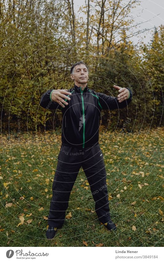 Übung "Stehen wie ein Baum" beim Qi Gong praktizieren auf der Wiese Qi gong fit Glück zufrieden Zufriedenheit Freude vital Sport Park Außenbereich Herbstfarben