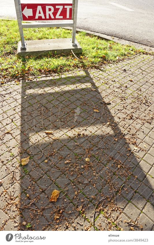 Rotes Hinweisschild "ARZT" wirft auf dem Fußweg einen Schatten / Orientierung / Wegweiser Arzt Pfeil Straße Schilder & Markierungen Wege & Pfade Zeichen