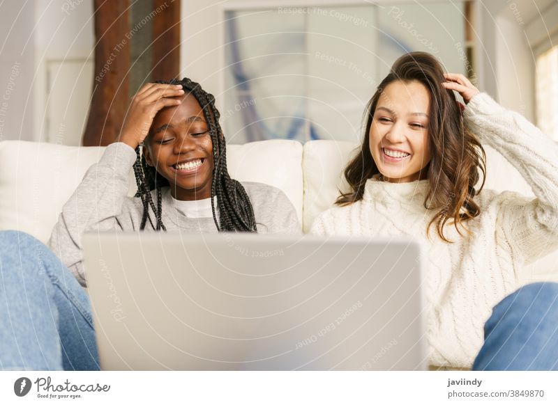 Zwei Studentinnen, die zu Hause mit einem Laptop auf der Couch sitzen. Frauen Freund multiethnisch Computer rassenübergreifend Liege Schüler schwarz Afro-Look