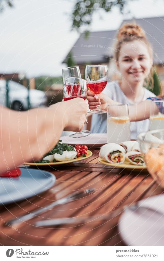 Familie macht Toast während des Sommers beim Abendessen im Freien in einem Hausgarten heimwärts Festessen habend Picknick Lebensmittel Mann Zusammensein Frau