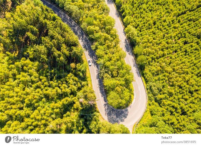 eine Waldstraßenkurve mit einem rasenden Auto von oben Straße kurvige Straße Wald von oben Straße von oben grün weiß weißes Cabrio PKW Bäume Baum