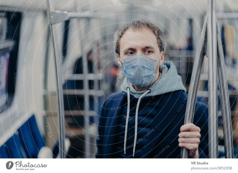 Foto eines männlichen Passagiers, der während einer U-Bahnfahrt während einer ansteckenden Krankheit eine Gesichtsmaske trägt, verhindert die Verbreitung des Coronavirus, posiert in öffentlichen Verkehrsmitteln, denkt über die Seuchensituation in seinem Land nach