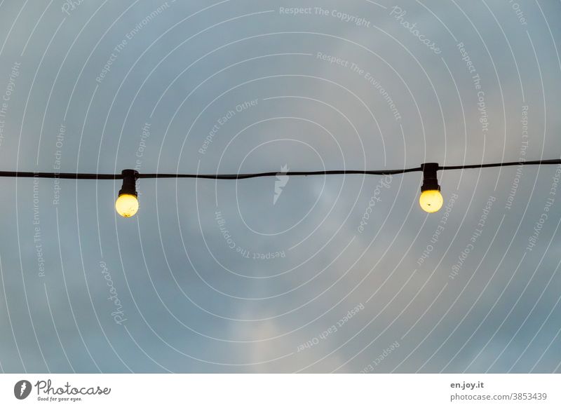 zwei leuchtende Glühbirnen hängen an einem Seil unter freiem Himmel mit Wolken Licht Lichter Beleuchtung Lampen Energie Abend Strom Dämmerung