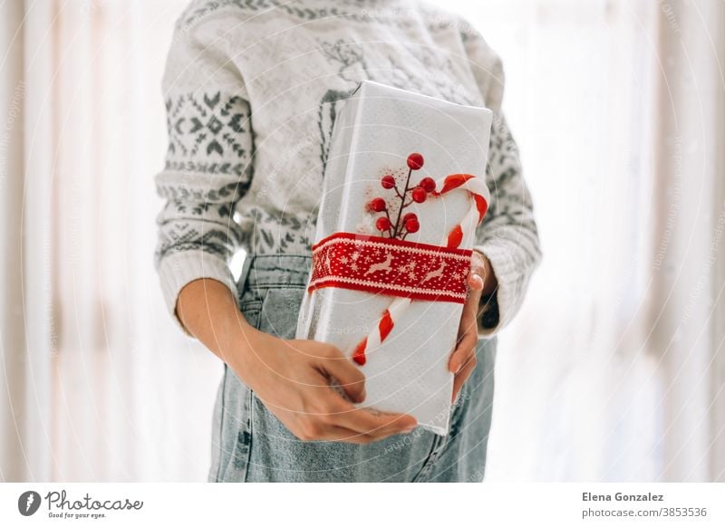 Junge, nicht wiedererkennbare Frau hält in einem Geschenkkarton aus Metallpapier mit rotem Zwirn und Süßigkeiten. Weihnachts-Silvester-Geschenk. Weihnachten