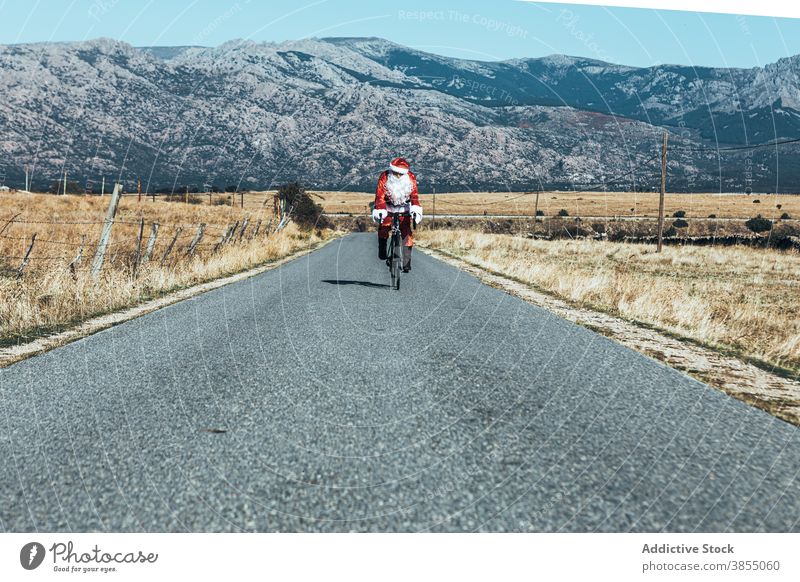 Weihnachtsmann auf dem Fahrrad entlang der Bergstraße Mitfahrgelegenheit Straße leer Berge u. Gebirge Tracht rot Farbe männlich modern Reise Freiheit