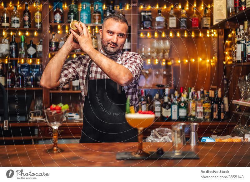 Fröhlicher Barmann, der einen Cocktail im Shaker mixt Mann Barkeeper schütteln mischen Glück Abfertigungsschalter Glas Arbeit männlich Lebensmitte reif Job