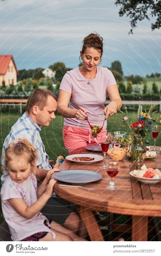 Familie isst während des Sommerpicknicks im Freien in einem Hausgarten zu Abend heimwärts Festessen habend Picknick Lebensmittel Mann Zusammensein Frau Kind