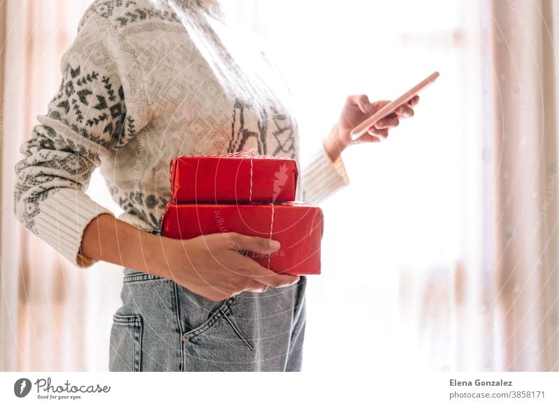 Junge unkenntlich beim Beobachten ihres Mobiltelefons Frau beim Beobachten ihres Mobiltelefons hält rote Geschenkkartons. Weihnachts-Silvester-Geschenk.