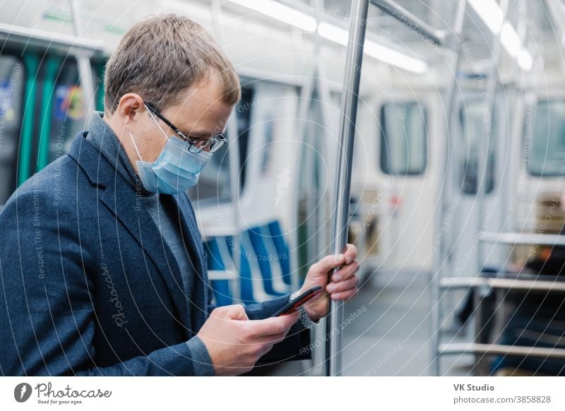 Ein seriöser Mann, der zur Arbeit in die U-Bahn pendelt, trägt eine Virenschutzmaske, da er in einer leeren U-Bahn oder Metro immer in Kontakt mit modernen zellularen Posen steht. Konzept der Entfernung. Öffentliche Verkehrsmittel während des Coronavirus