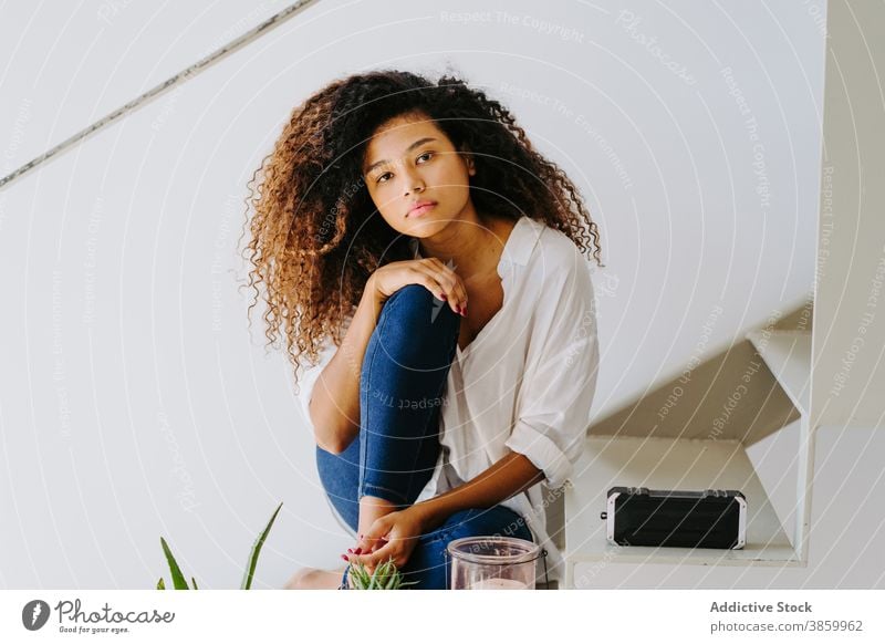 Stilvolle ethnische Frau mit lockigem Haar sitzt auf Stufen zu Hause krause Haare Afro-Look trendy Treppe Windstille sich[Akk] entspannen modern attraktiv jung