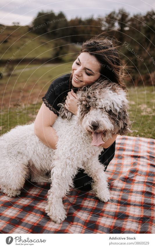 Lächelnde Frau umarmt Hund in der Natur Besitzer kuscheln Freundschaft spanischer Wasserhund Zusammensein Umarmung genießen Decke Wochenende Haustier Tier