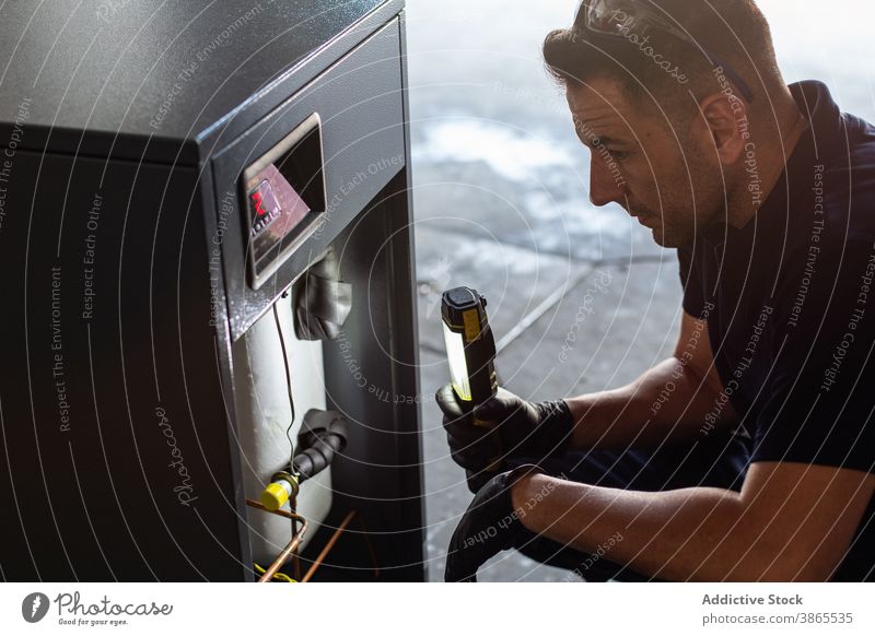 Mechaniker mit Taschenlampe, der den Mechanismus in der Werkstatt untersucht untersuchen prüfen Reparatur Arbeit Maschine Werkzeug Mann Licht professionell