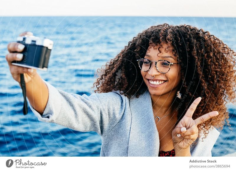 Glückliche afroamerikanische Frau nimmt Selfie in der Nähe von Meer MEER Lächeln Wochenende v-Zeichen Fotoapparat gestikulieren Wasser Ufer jung ethnisch