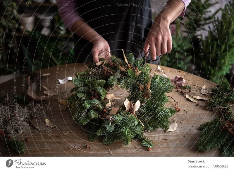 Frau macht Weihnachtskranz aus Fichtenholz, Schritt für Schritt. Konzept der Arbeit des Floristen vor den Weihnachtsfeiertagen. Hand Herstellung Hände Holztisch