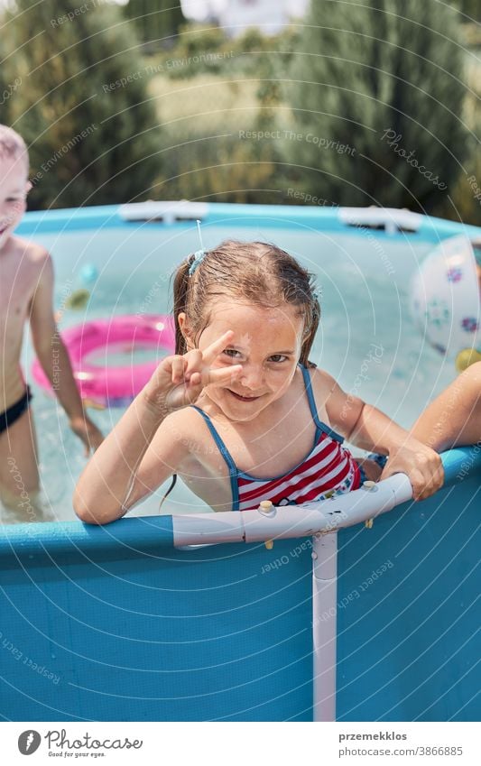 Glückliches Mädchen macht V-Zeichen-Geste und spielt in einem Pool und genießt das Plantschen und den Spaß mit den Geschwistern an einem sonnigen Sommertag