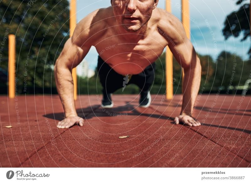 Junger hemdloser Bodybuilder macht Liegestützen auf rotem Gummiboden während seines Trainings in einem modernen Calisthenics-Straßentrainingspark calisthenics